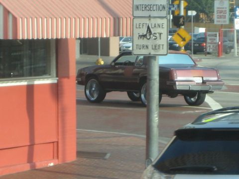 1968 Ford Mustang - Maroon coupe with large chrome wheels seen from the rear on a city street.