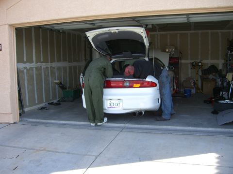 1996 Ford Probe - Three people work on a white coupe in a garage, with the trunk and hood open.