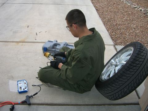1996 Ford Probe - A person in a green jumpsuit sits on concrete, using a rotary tool to work on a tire and rim assembly.
