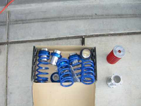 1996 Ford Probe - Suspension parts laid out on a concrete surface, including blue coil springs and adjustable perches.