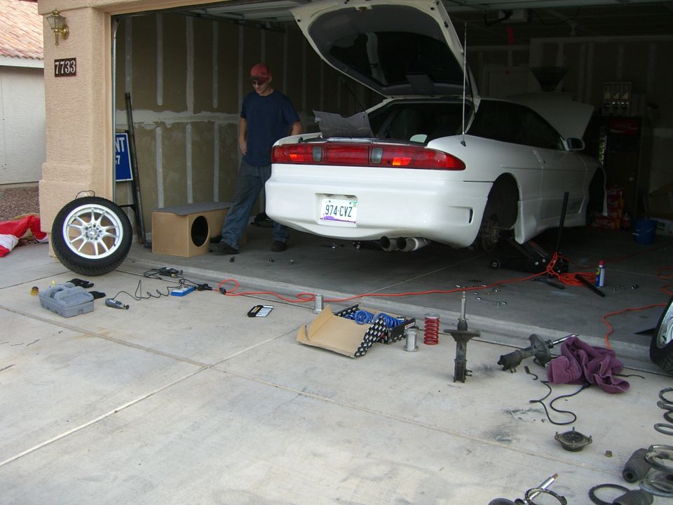 White coupe rear view, trunk open, parts on garage floor