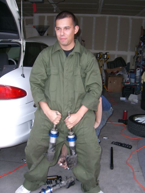 1996 Ford Probe - A man holds car suspension parts while working on a white vehicle in a garage.