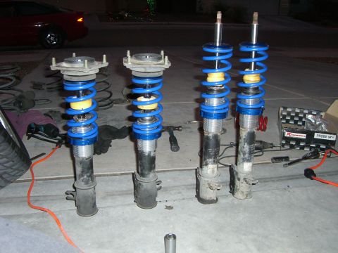 1996 Ford Probe - Several car suspension assemblies are laid out on the ground, with tools and a box nearby.