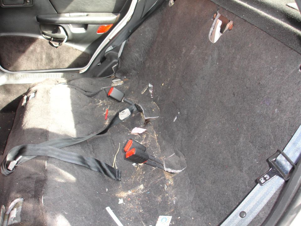 Car interior showing removed rear seats, exposed carpet, and seatbelts
