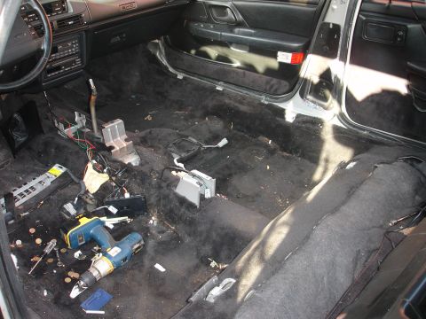 1993 Ford Taurus - The interior of a car is shown with the carpet and seats removed, revealing wiring and tools.
