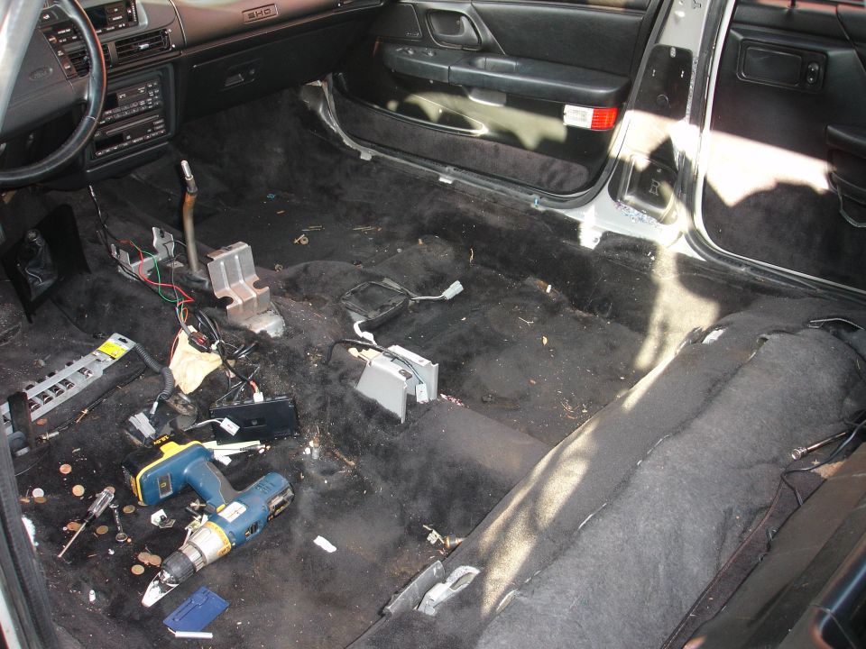 Gutted car interior floor with carpet pulled and a cordless drill during work