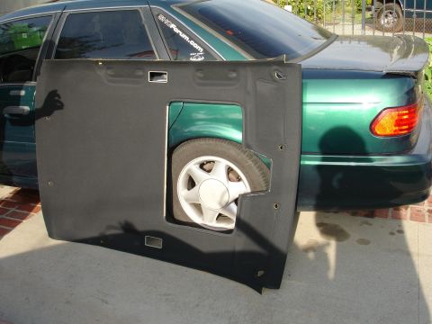 1993 Ford Taurus - Removed black interior panel from a green sedan, revealing the rear wheel.