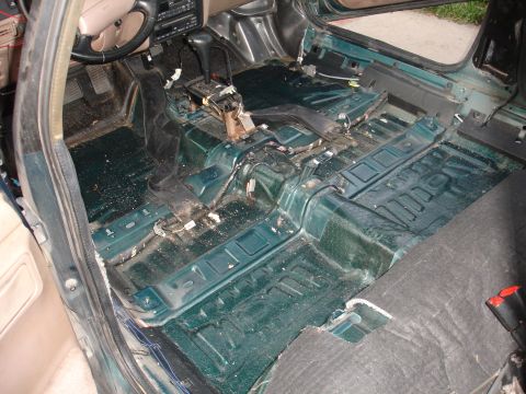 1993 Ford Taurus - The interior of a car has been stripped down, revealing the floor pan and exposed wiring.