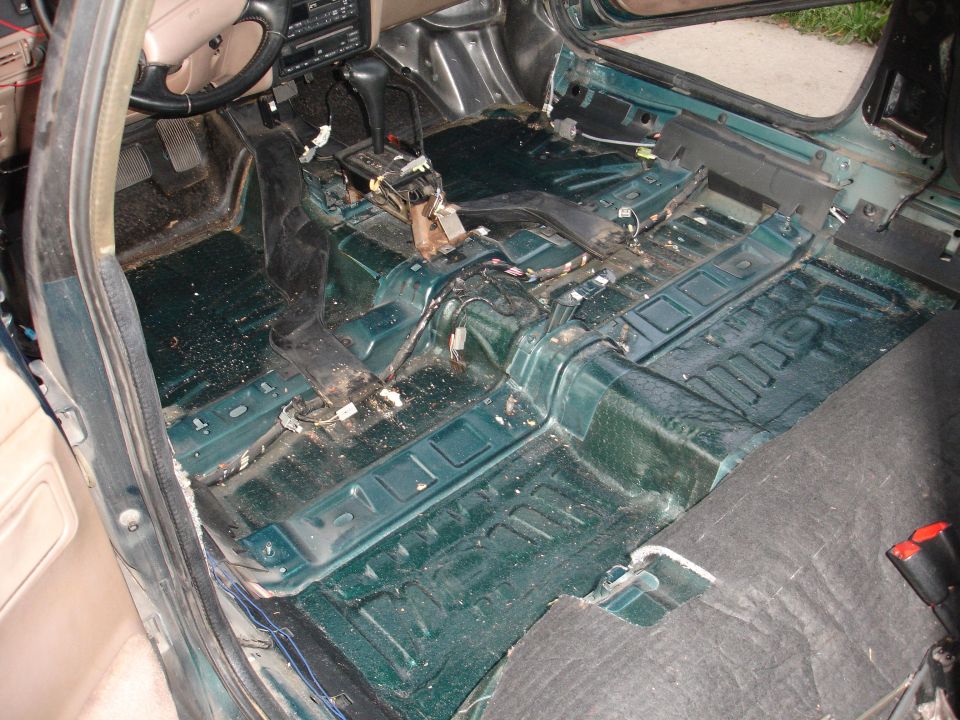 Interior of a car with seats and carpet removed, showing the bare floor and center console