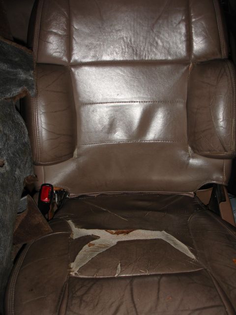 1993 Ford Taurus - A worn brown leather car seat shows significant damage to the upholstery, revealing underlying material and a red seatbelt buckle.
