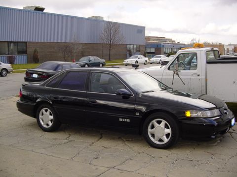 1998 Ford Taurus - A black 1998 Ford Taurus sedan is parked next to a white truck.