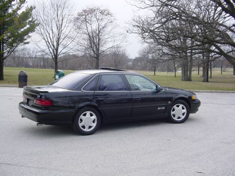 1998 Ford Taurus - This 1998 Ford Taurus is parked in a lot with trees in the background.