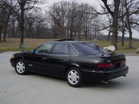 1998 Ford Taurus - A black sedan is parked outdoors on a cloudy day, with trees and a grassy hill visible behind it.