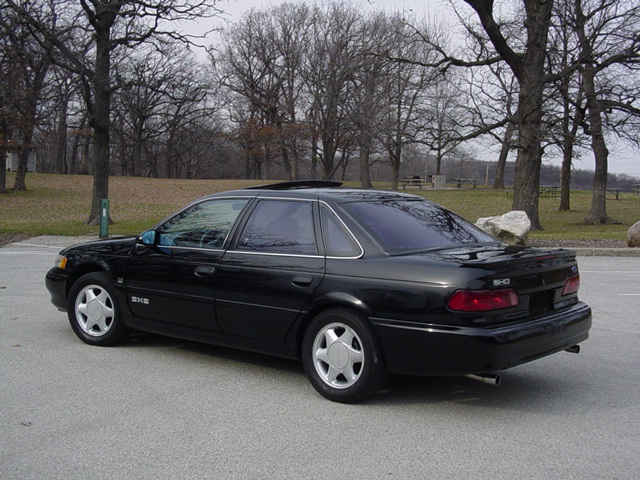 Black sedan parked on pavement with trees in background. Has a sunroof and silver wheels