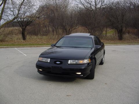 1998 Ford Taurus - This black 1998 Ford Taurus is shown in a parking lot with bare trees in the background.