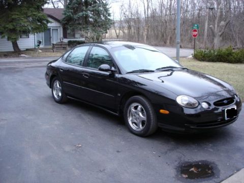 1998 Ford Taurus - A black sedan is parked on a driveway in front of a house.