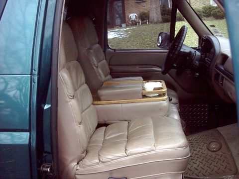 1996 Ford Bronco - Interior of a teal Ford truck/Bronco shot through the open passenger door, showing tan leather captain-style bucket seats with a wood-trimm…