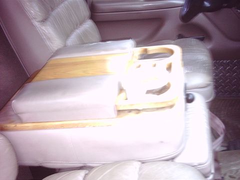 1996 Ford Bronco - Close, slightly blurred interior shot of a truck's tan leather center jump seat/console with a shop-built wooden cupholder tray laid across…