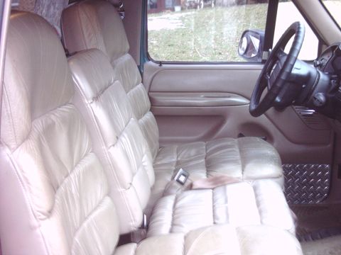 1996 Ford Bronco - Passenger-side interior view of a tan leather cabin with pleated bucket seats, tan door panel with recessed pull, black steering wheel and…