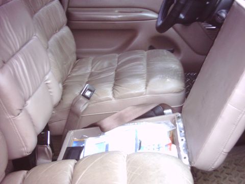 1996 Ford Bronco - Interior shot looking across a tan leather cabin at pleated captain's chairs and a center console with its lid flipped open to show the sto…