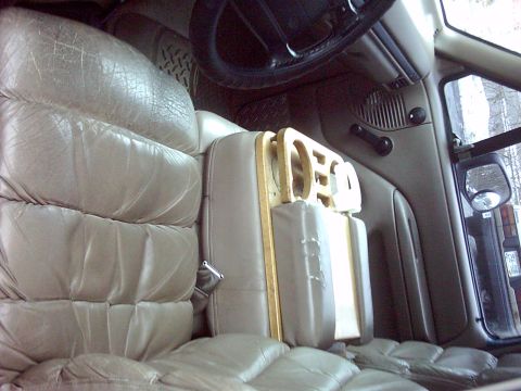 1996 Ford Bronco - Interior close-up of tan pleated leather seats with a shop-built bare MDF/particleboard cup-holder or console panel wedged beside the passe…