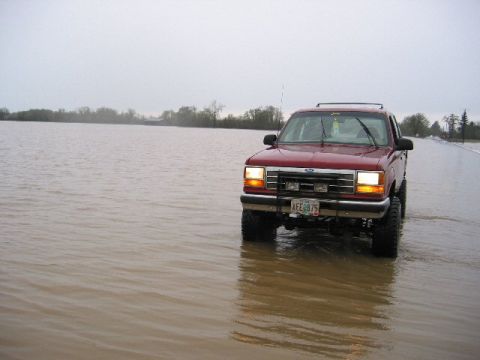 1991 Ford Explorer - A red 1991 Ford Explorer navigates through flooded terrain under an overcast sky.