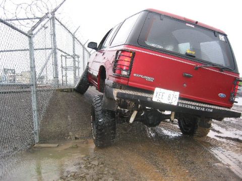 1991 Ford Explorer - This lifted 1991 Ford Explorer is navigating a muddy, uneven terrain next to a fenced area.