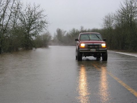 1991 Ford Explorer - A red 1991 Ford Explorer navigates through flooded conditions on a road, with trees and brush visible on the side.
