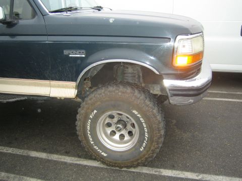 1990 Ford Bronco - Close-up of a dark green lifted Ford Bronco's front fender, headlight and BFGoodrich Mud-Terrain T/A tire on a chrome wheel in a parking lo…
