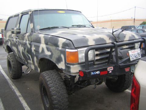 1990 Ford Bronco - camo-painted lifted Ford Bronco with a black tube grille guard and ARB front bumper, California plate 5C1W69B, parked in a lot.