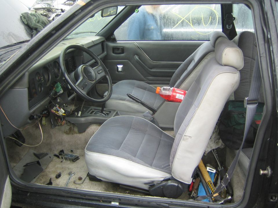 Gray cloth bucket-seat interior of an older car viewed through the open driver door