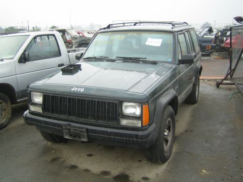 1990 Ford Bronco - green Jeep Cherokee with hood scoop and alloy wheels sits in a fenced salvage yard.
