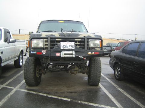 1990 Ford Bronco - lifted camouflage truck shows its exposed front axle, brush guard, Warn winch and California plate 5CHW698 in a parking lot.