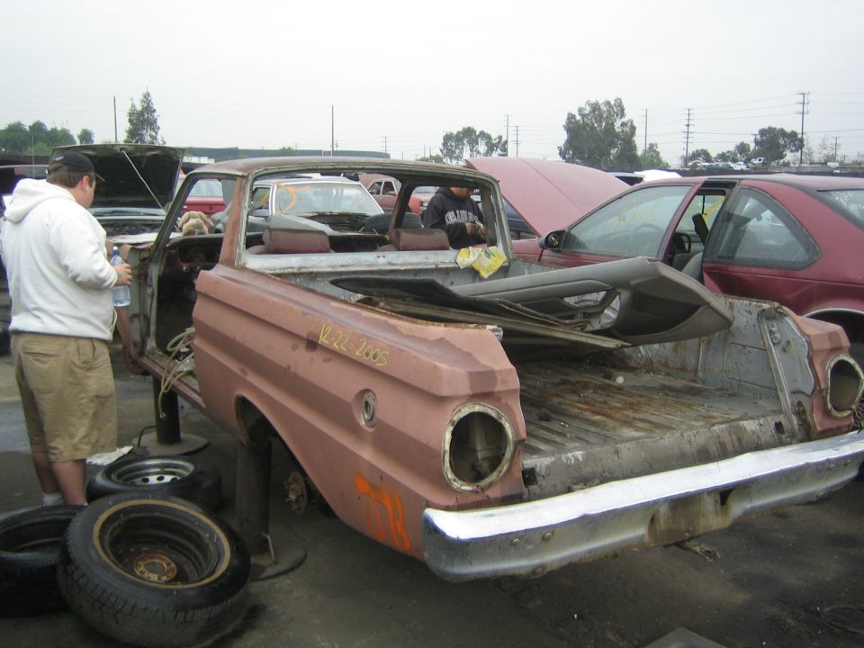 Rusty pink Ford Ranchero car-pickup being stripped in a salvage yard