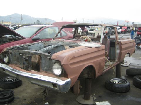 1990 Ford Bronco - pink Ford Ranchero sits partly disassembled with bare front end and a teddy bear perched on the cowl in a salvage yard.
