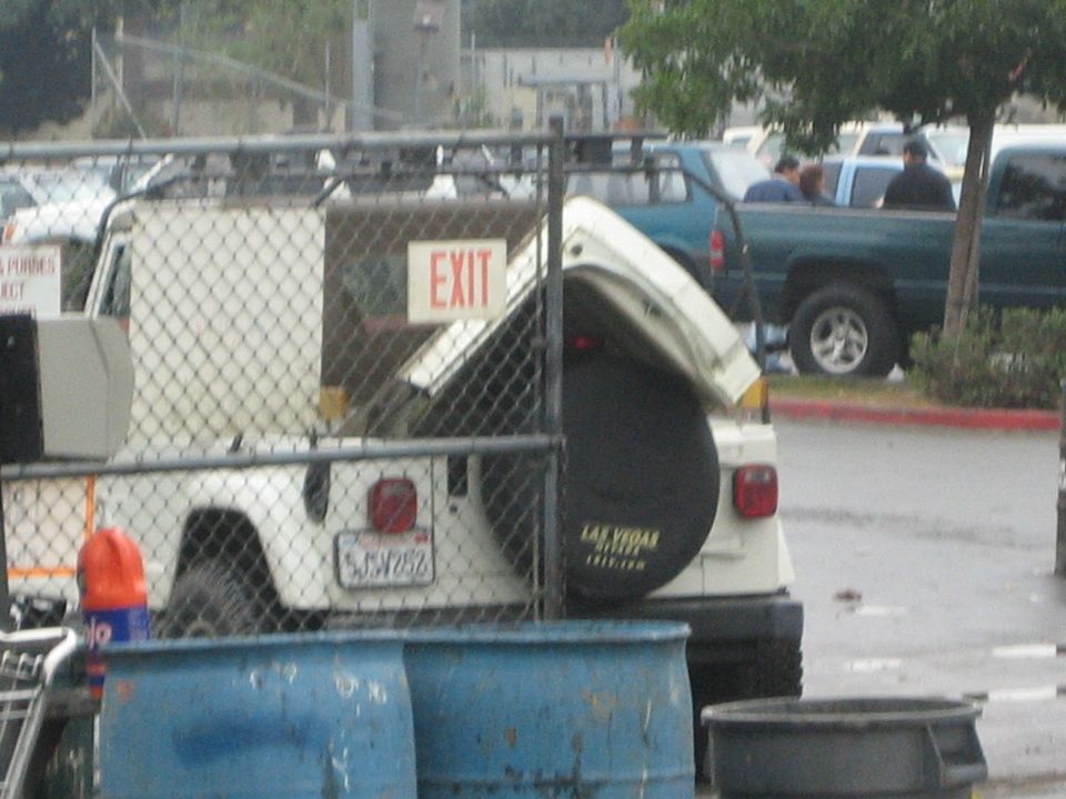 White Hummer with open rear hatch behind a chain-link fence, plate 6JSW262