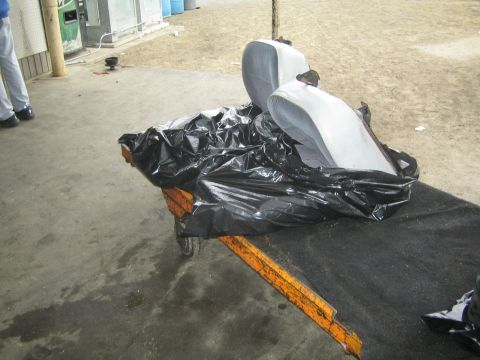 1990 Ford Bronco - Two gray car seats rest atop black plastic sheeting on an orange rolling cart in a paved yard.