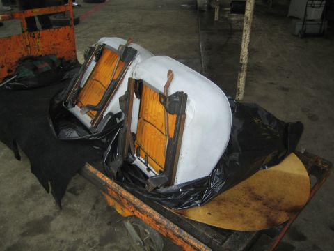 1990 Ford Bronco - Two white car seats lie inverted on black plastic over an orange cart, exposing their orange seat track frames indoors.