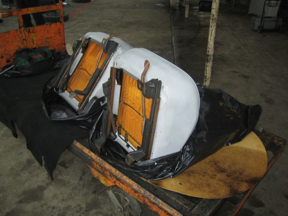 Two white vehicle seats turned upside down showing track frames on an orange cart