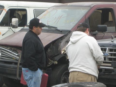 1990 Ford Bronco - Two men examine the crumpled front end of a maroon van with a Ford emblem in an outdoor lot.