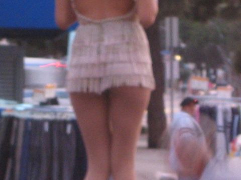 1990 Ford Bronco - Close rear view of a person in a short cream fringed dress standing on a street with clothing vendor stalls behind.
