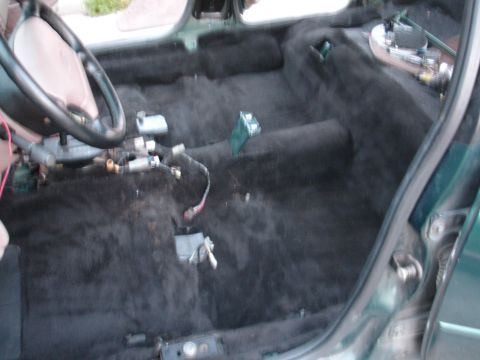 1993 Ford Taurus - The interior of a car is shown with the carpet removed, revealing exposed wiring and the steering wheel.