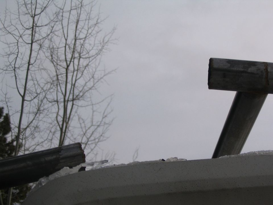 Bent icy metal roll bar tubing against gray winter sky above a light body panel