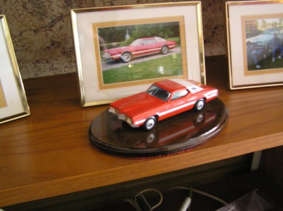 1972 Ford Ranchero - A red 1972 Ford Ranchero model car is displayed on a wooden base, with framed photos in the background.