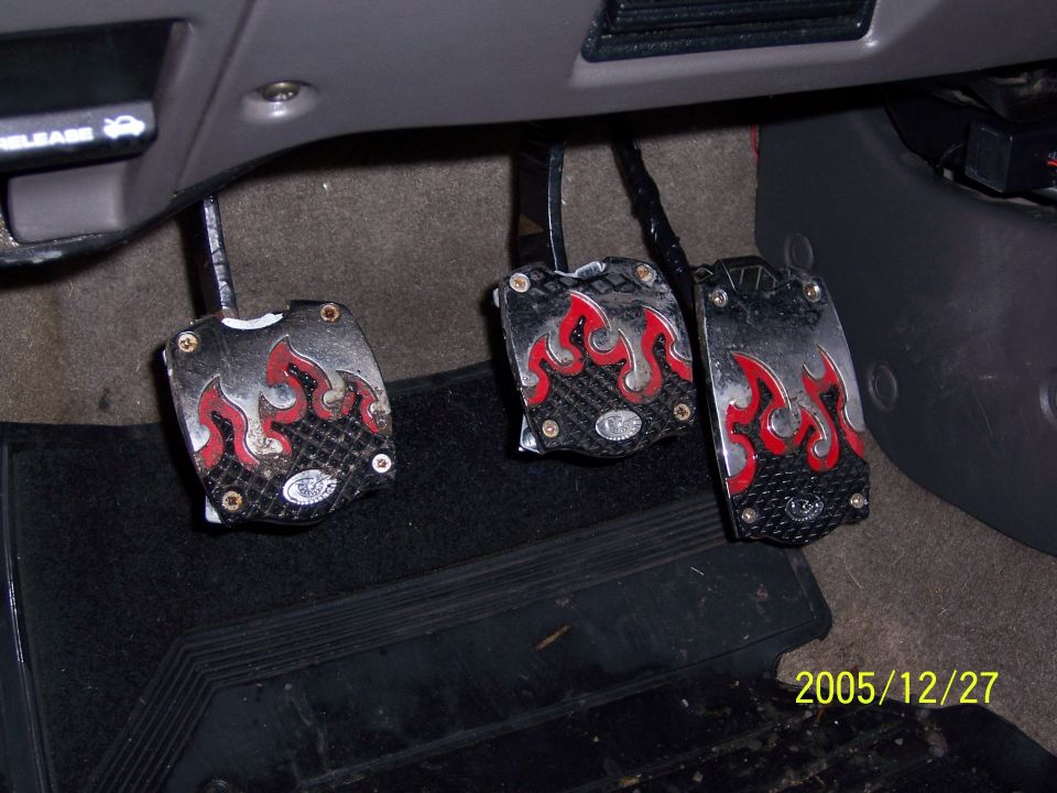 Three aftermarket flame-design pedal covers on clutch, brake and gas pedals in a car's footwell
