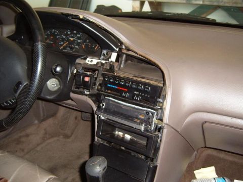 1993 Mazda MX-6 - The interior of a car shows a disassembled dashboard with the radio missing and climate controls exposed.