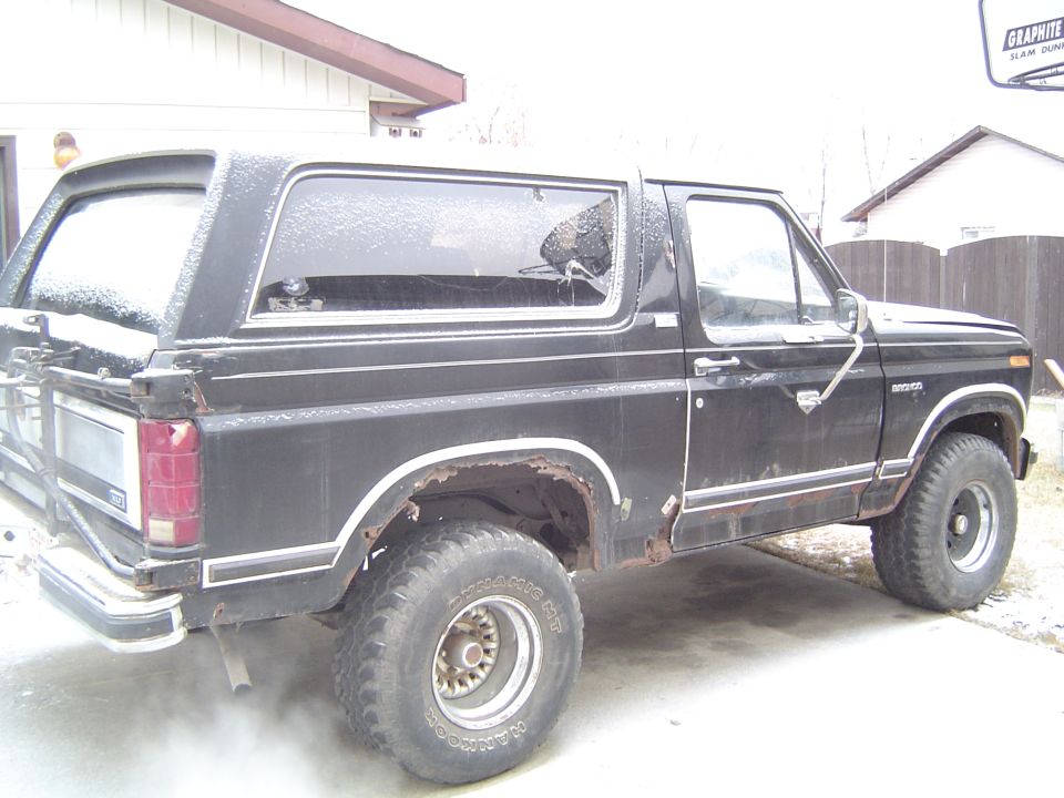 Black Ford Bronco SUV, passenger side, lifted on large Hankook mud tires, rust on rear fender, snowy driveway