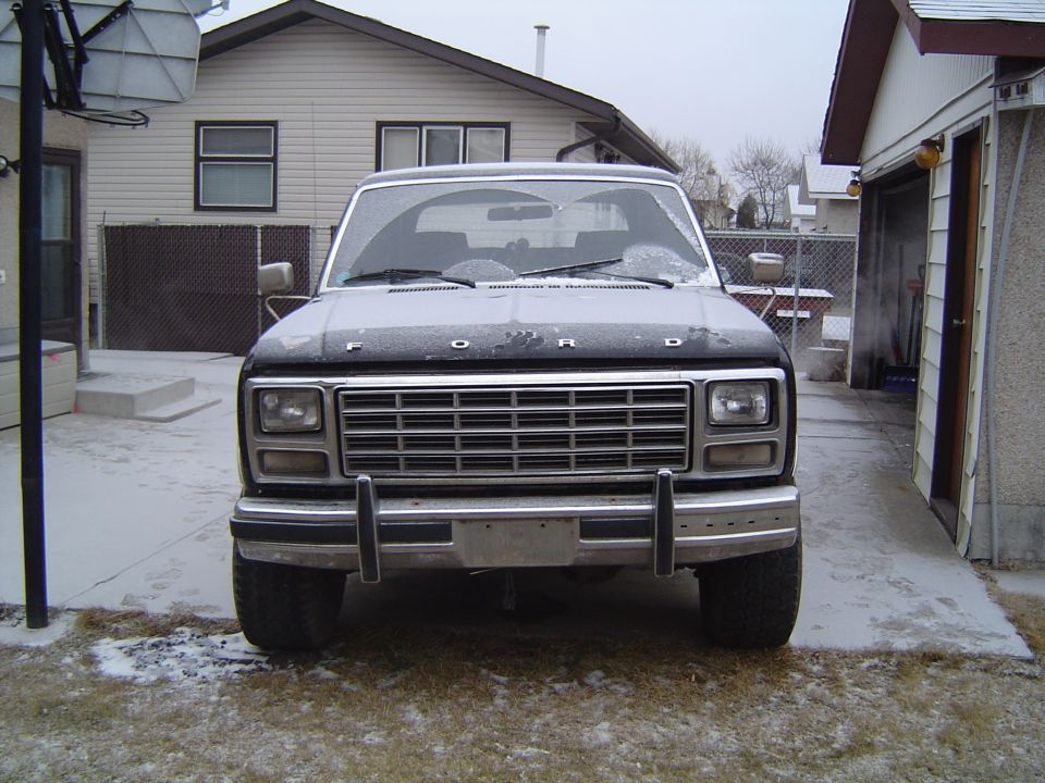 Front view of a frost-covered dark Ford truck with chrome grille and bumper parked in a snowy driveway
