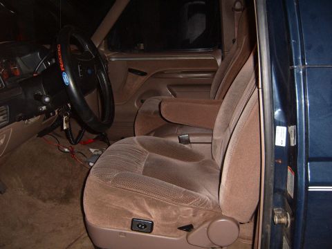 1993 Ford Bronco - The interior of a blue SUV features brown fabric seats and a dark steering wheel with a racing cover.