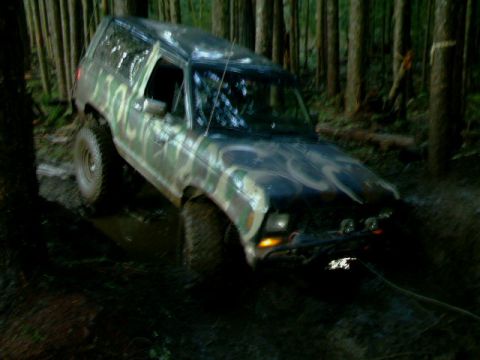 1987 Ford Bronco II - A 1987 Ford Bronco II navigates a muddy trail through a dense forest.
